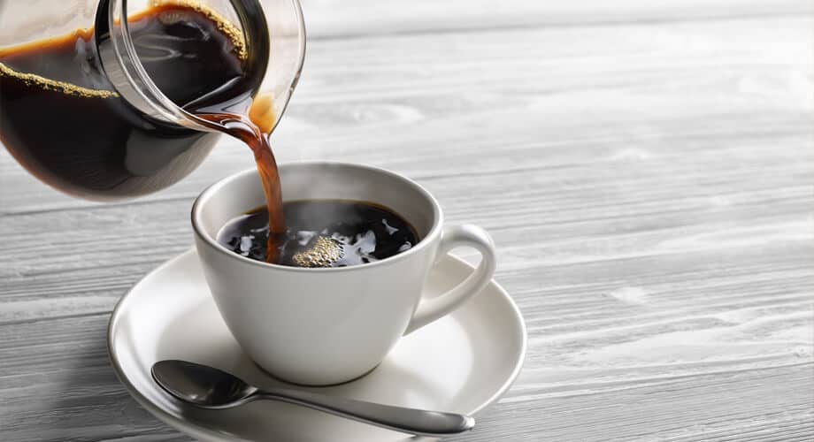 Café tem glúten? Imagem com café preto sendo servido em uma xícara branca, sob um pires branco com colher prata.