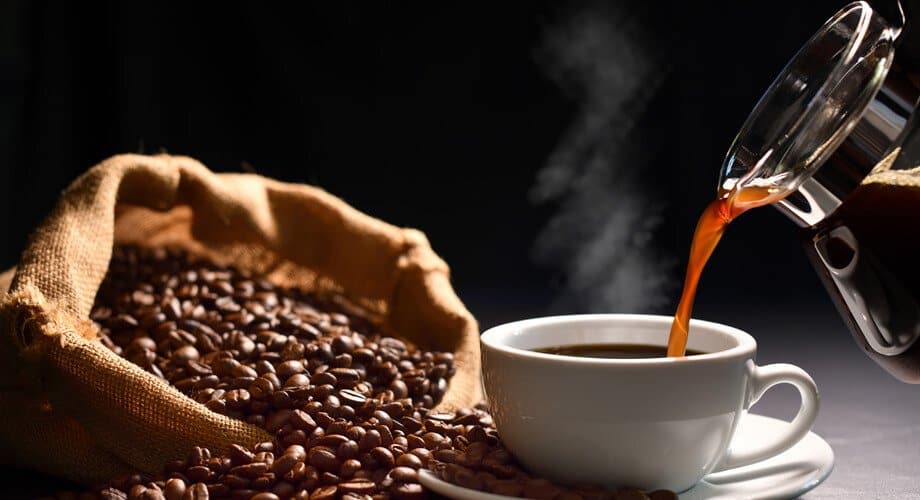 Para que serve o café: xícara sendo completada com café ao lado de grãos de café