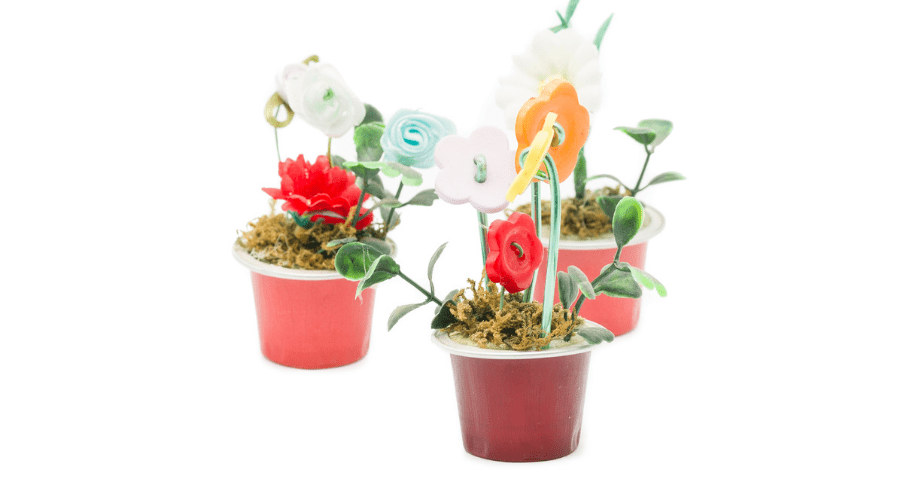 Conjunto de vasos feitos através de artesanato com cápsulas de café, preenchidos com terra e flores artificiais.