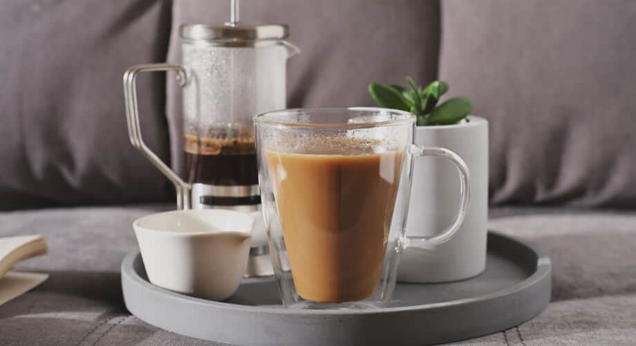 café com leite condesado servido em uma bandeja redonda cinza, junto com um vaso de suculenta