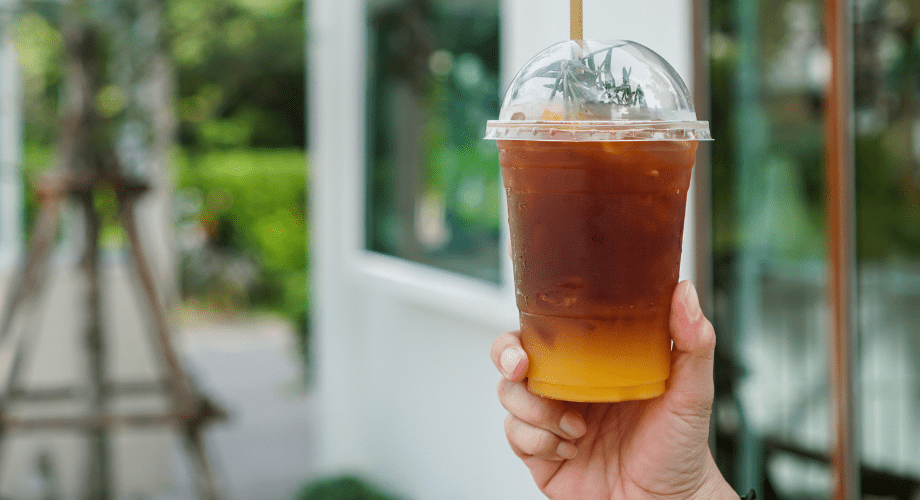 Mão segura um copo descartável transparente cheio de café com suco de laranja