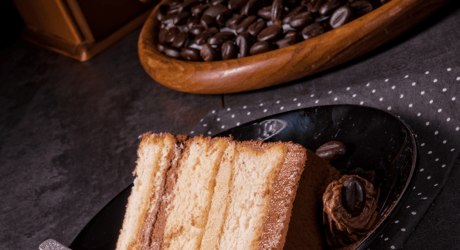 Receitas simples de torta de café: aprenda aqui! Pedaço de torta de café servido em um prato preto ao lado de grãos de café