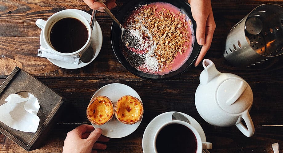 mesa de café em portugal com pastéis de belém, duas xícaras de café e um iogurte