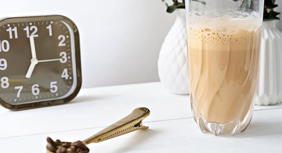 imagem de um smoothie de café ao lado de um relógio e um moedor com grãos de café em cima