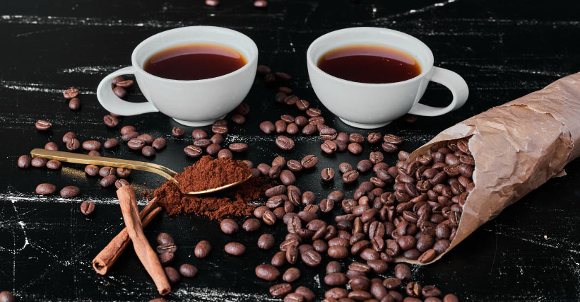 Café gourmet ou especial? Saiba a diferença entre os dois Café gourmet ou especial - Sobre uma mesa, estão duas xícaras de café, um saco de café em grãos, uma lasca de canela e uma colher com café em pó.
