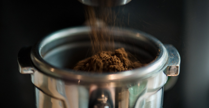 moedor de café manual ou eletrico - Café moído sendo depositado em um porta-filtro de máquina de espresso, destacando o processo de moagem.