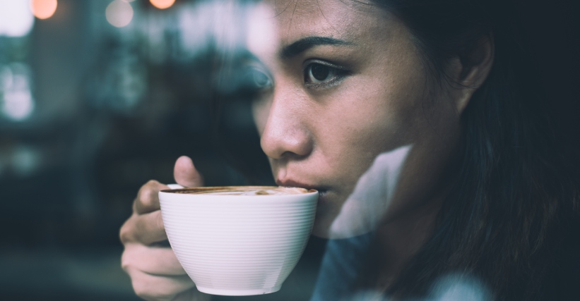 Cafie da ansiedade - Mulher pensativa tomando uma xícara de café em ambiente interno, representando a relação entre o consumo de café e a ansiedade.